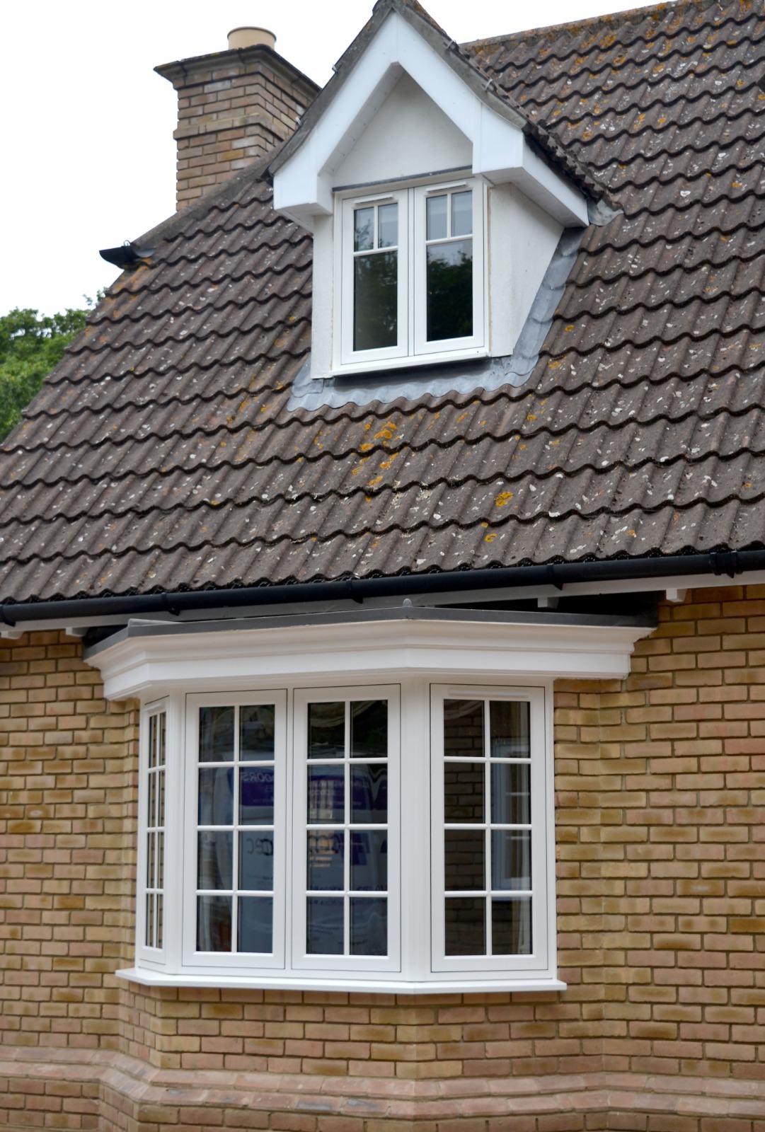 White uPVC bay window and matching dormer window with Georgian glazing bars on a yellow-brick detached house